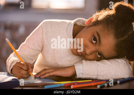 Close-up Portrait von liebenswert afroamerikanische Mädchen zeichnen mit Bleistift und Blick in die Kamera, macht Hausaufgaben Konzept Stockfoto