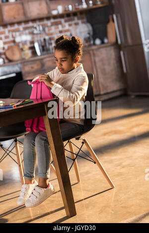 Niedliche kleine Mädchen Rucksack beim Sitzen am Tisch mit Filzstift Stifte halten tun Hausaufgaben Konzept Stockfoto