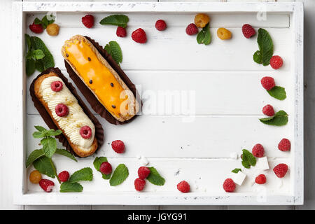 Weißes Holztablett mit französischer Eclairs und Beeren Stockfoto