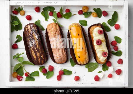 Weißes Holztablett mit französischer Eclairs und Beeren Stockfoto