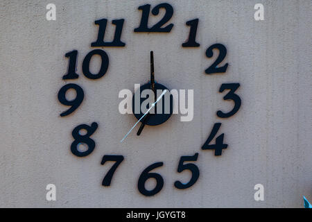 Große Uhr auf weißen Wand mit schwarzen Zahlen. Stockfoto