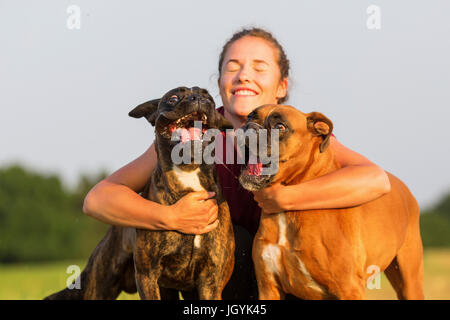 junges Mädchen umarmt zwei Boxer-Hunde auf einem Feldweg Stockfoto