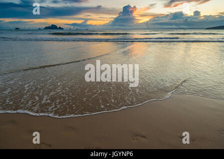 Fußspuren im Sand am Rande des Strandes und der Sonnenuntergang am Horizont Stockfoto