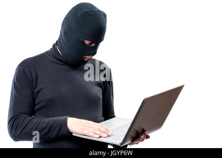 Ein Hacker in schwarzer Kleidung und eine Maske mit einem Laptop auf einem weißen Hintergrund Stockfoto