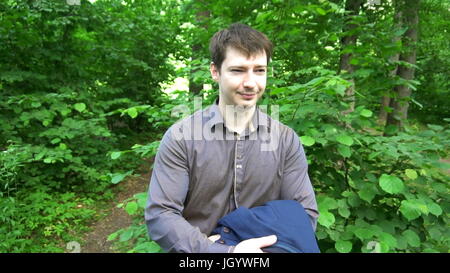 ein junger Mann im Wald steht, wirft die Jacke über seine Schulter. Stockfoto