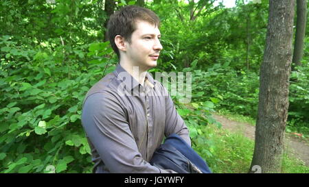 ein junger Mann im Wald steht, wirft die Jacke über seine Schulter. Slow-Motion. Stockfoto