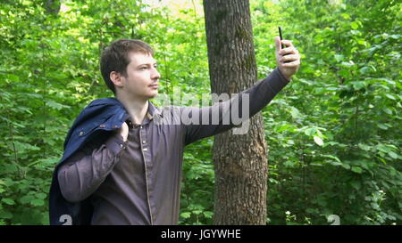 ein junger Mann im Wald steht, wirft die Jacke über die Schulter und macht ein Selbstporträt. Slow-Motion. Stockfoto