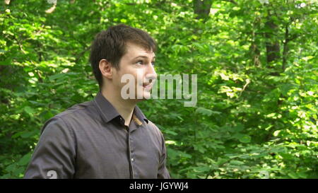 ein junger Mann im Wald steht, wirft die Jacke über die Schulter und macht ein Selbstporträt. Slow-Motion. Stockfoto