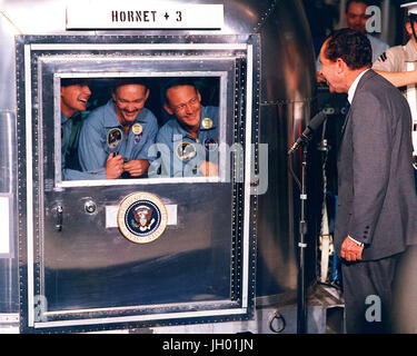 Präsident Richard M. Nixon begrüßt die Apollo 11 Astronauten an Bord der USS Hornet, das Recovery-Schiff für die historische Mission der Apollo 11 Mondlandung. Beschränkt auf Mobile Quarantäne Facility (MQF) sind Neil A. Armstrong, Kommandant; Michael Collins, Befehl Modul-Pilot; und Edwin E. Aldrin Jr., Pilot der Mondlandefähre. Stockfoto