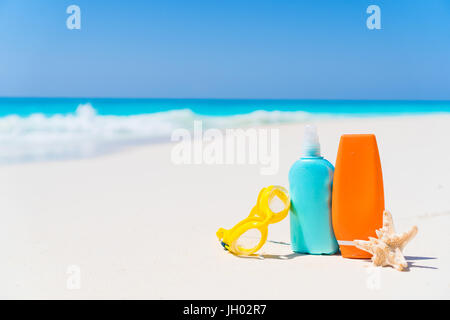 Sonnencreme-Flaschen, Schutzbrillen, Seesterne am weißen Sandstrand Hintergrund Ozean Stockfoto