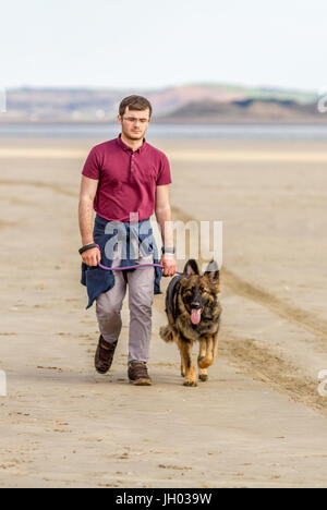 Junge Teenager männlich zu Fuß Deutscher Schäferhund auf leeren Sandstrand Stockfoto