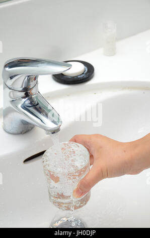 Füllt ein Glas mit Wasser unter dem Wasserhahn Stockfoto