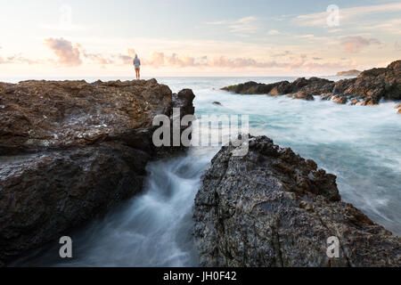 Eine Person Uhren den Sonnenaufgang über dem Meer in einer wunderschönen felsigen Seelandschaft Szene in Port Macquarie, Australien. Stockfoto