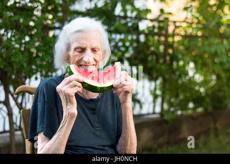 Fröhliche Oma Essen Wassermelone Frucht im Hinterhof Stockfoto