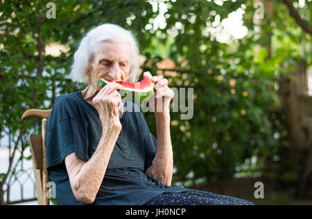 Ältere Frau Essen Wassermelone Frucht im Hinterhof Stockfoto