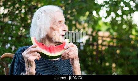 Ältere Frau Essen Wassermelone Frucht im Hinterhof Stockfoto