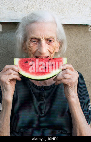 Ältere Frau Essen Wassermelone Frucht im Hinterhof Stockfoto