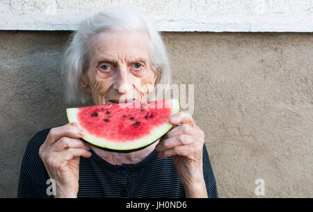 Fröhliche Oma Essen Wassermelone Frucht im Hinterhof Stockfoto