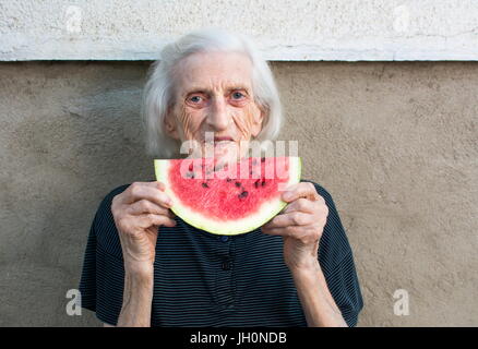 Ältere Frau Essen Wassermelone Frucht im Hinterhof Stockfoto