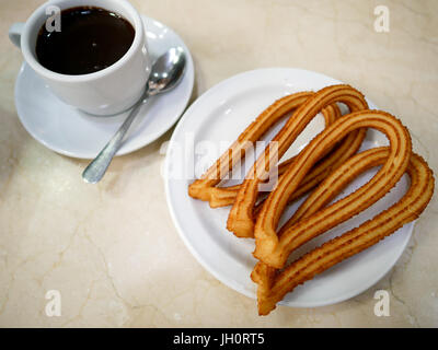 Churros oder Spanisch gebraten - Teig Gebäck auf weiße Platte serviert mit einer Tasse heißer Schokolade als Soße. Stockfoto