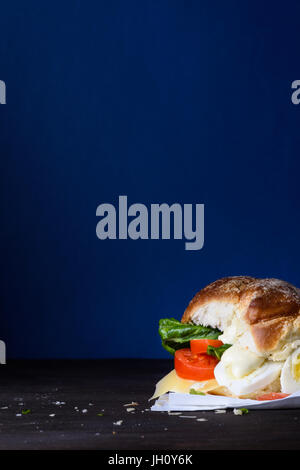 Veggie-Ei-Burger mit Käse und Tomaten auf einer Arbeitsplatte, blauer Hintergrund, Textfreiraum. Stockfoto