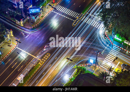 Bangkok, Thailand - 6. Juli 2017 - zeigt eine Straßenkreuzung in Bangkok in einer regnerischen Nacht, Autos und Motorrad gehen über ihr Geschäft auf Ju Stockfoto