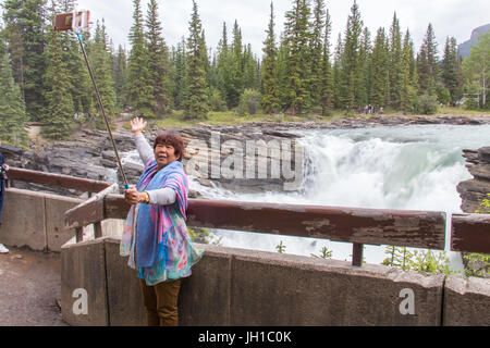 Eine Frau ist posiert und nehmen ein Selbstporträt mit einem Selfie-Stick an den Anthabasca Falls, Jasper Nationalpark, Alberta, Kanada Stockfoto