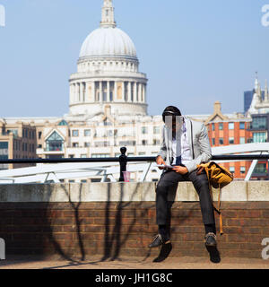 UK, London - 8. April 2015: ein unbekannter Mann sitzt auf dem Hintergrund der St. Pauls Kathedrale in London lesen Stockfoto