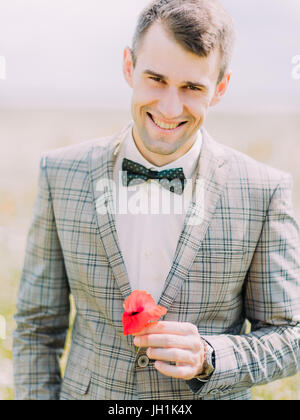 Das Close-up Portrait von der lächelnden Bräutigam hält des Mohns. Stockfoto