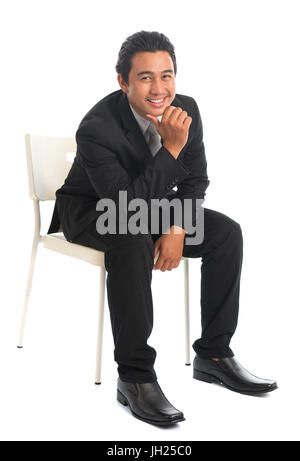 Voller Körper attraktiveren jungen Südost asiatischen Geschäftsmann auf Stuhl sitzend, hand am Kinn, isoliert auf weißem Hintergrund. Asiatische malaiischen Männermodel. Stockfoto