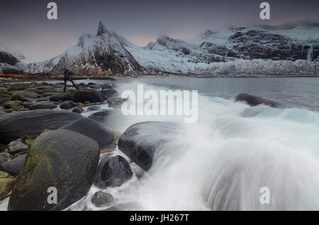 Fotograf auf den Felsen, umgeben von schneebedeckten Gipfeln und Wellen von den kalten See, Senja, Ersfjord, Troms Grafschaft, Norwegen Stockfoto