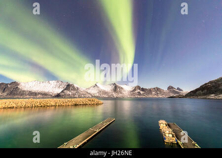 Nordlichter auf schneebedeckten Gipfeln und eisigen Meer entlang Mefjorden gesehen aus dem Dorf Mefjordvaer, Senja, Troms, Norwegen Stockfoto