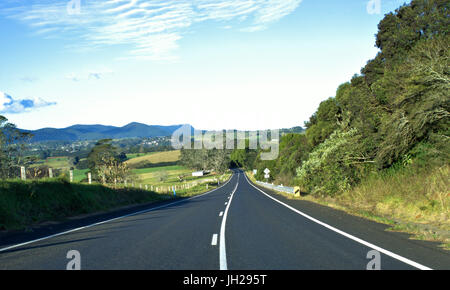 Schöne Landstraße mit grünem Rasen, Bäumen und blauen Himmel und Berge oben im Hintergrund in New South Wales Australien Stockfoto