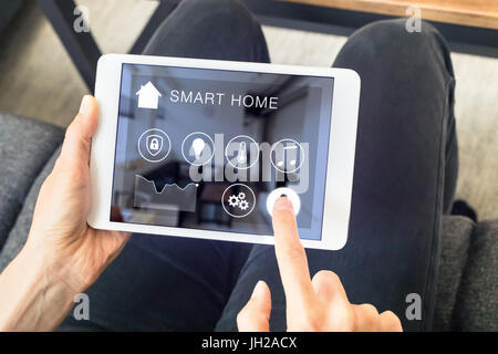 Person mit smart home automation Assistant auf einem digitalen Tablet Computer angeschlossenen Geräte im Zimmer zu steuern Stockfoto