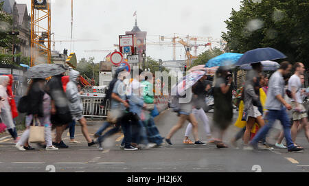 Berlin, Deutschland. 12. Juli 2017. Menschen tragen Regenschirme und Regen, die Umhänge zu über die Straße Unter Den Linden, Fuß während es beginnt zu regnen in Berlin, Deutschland, 12. Juli 2017 tragen. Rotes Rathaus (Rotes Rathaus) können im Hintergrund zu sehen. Foto: Wolfgang Kumm/Dpa/Alamy Live News Stockfoto