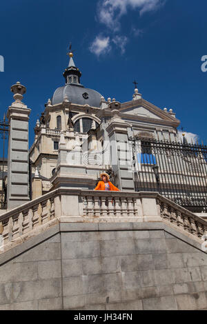 Frau trägt leuchtend orange oben auf der Treppe, die Almudena-Kathedrale in Madrid Spanien, mit blauem Himmel oben Stockfoto