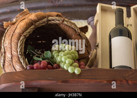 Bunte Weintraube in Wodden Korb und Weinflasche mit seiner Box im Regal Stockfoto