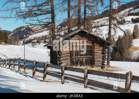 Kleine Holzhütte und Zaun unter Bäumen im Wintertag mit frischem Schnee in den Bergen Stockfoto