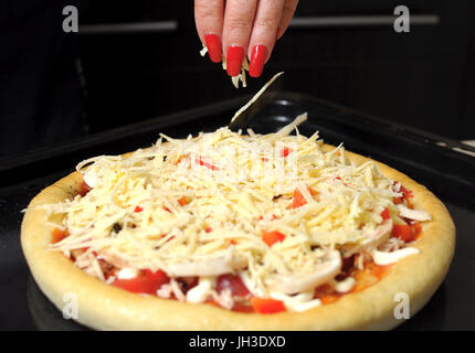 Eine weibliche Hand streut eine Pizza mit geriebenem Käse Nahaufnahme. Selektiven Fokus. Stockfoto