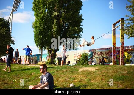 Eine junge Frau sitzt auf einer Schaukel s vor Graffiti auf einem verbliebenen Teil der ehemaligen Berliner Mauer am Mauerpark (Wand Parc) in Berlin am 18. Juni 2017. Dieses Bild ist Teil einer Serie von Fotos über den Tourismus in Berlin. Foto: Wolfram Steinberg/Dpa | weltweite Nutzung Stockfoto