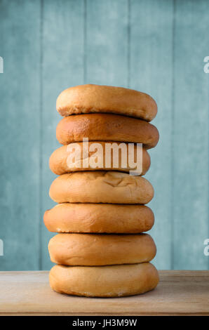 Einen hohen Stapel von ganze Bagels auf ein leichtes Schneidbrett aus Holz mit einem türkis blau Planke Hintergrund. Stockfoto