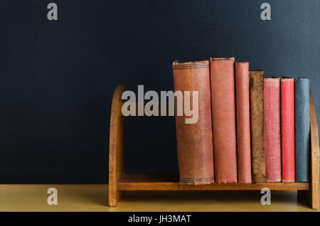 Eine Reihe gebrauchte von alten Bücher mit leeren Buchrücken, aufrecht auf einem Desktop-Regal mit schwarzen Tafel Hintergrund. Stockfoto