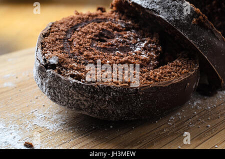 Nahaufnahme von geschnittene Schokolade Weihnachten Yule Log oder Biskuitrolle Kuchen.  Bestäubt mit Puderzucker, die auf hölzernen Schneidebrett verschüttet hat. Stockfoto