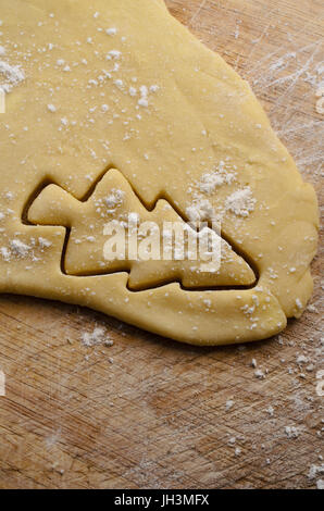 Weihnachtsbaum-Form aus Keks oder Cookie-Teig, auf alten hölzernen Schneidebrett mit verstreuten Mehl Streusel ausgeschnitten. Stockfoto