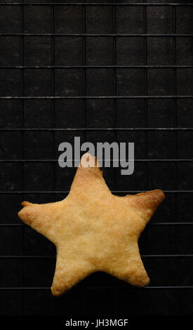 Overhead Schuss eines einzigen, unvollkommene Sterne Weihnachten Plätzchen geformt, frisch gebacken und platziert auf einem schwarzen Draht Rack-Kühlung. Stockfoto