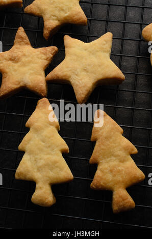 Overhead Schuss aus einer Auswahl von Weihnachtsgebäck im Baum und Stern Formen, frisch gebacken und auf einem schwarzen Draht Rack-Kühlung. Stockfoto