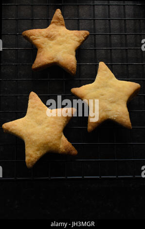 Overhead Schuss von drei sternförmig, gebacken nach Hause Weihnachten Kekse (Cookies) auf einem schwarzen Draht Rack-Kühlung. Stockfoto