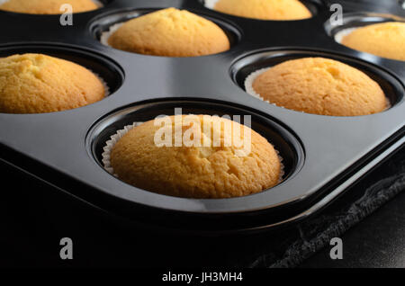 Backen Wohnkonzept mit mehreren Vanille Cupcakes in Papier Fällen innen Brötchen Zinn, Kühlung auf schwarzem Schiefer. Stockfoto