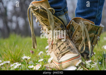Frau die gekreuzte Füße mit Turnschuhen, umgeben von kleinen Wiesenblumen. Stockfoto