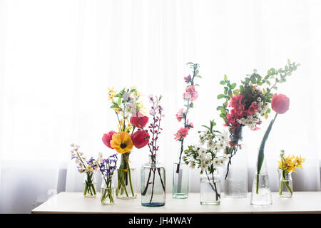Verschiedene schöne Blumen in Gläser mit Wasser auf dem Tisch neben dem Fenster Stockfoto